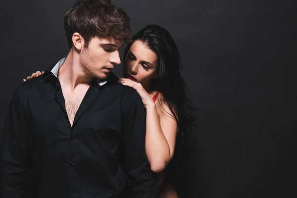 Atractiva mujer tocando guapo novio aislado en negro - foto de stock