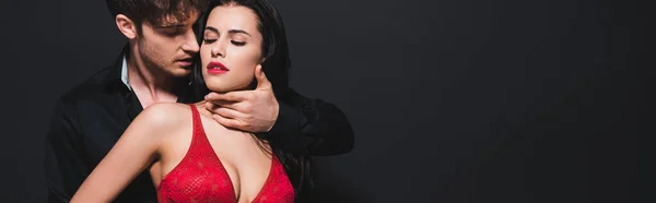 Tiro panorámico de hombre apasionado tocando chica sexy en sujetador rojo aislado en negro - foto de stock