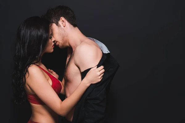Mulher apaixonada em lingerie vermelha despir o homem isolado no preto — Fotografia de Stock