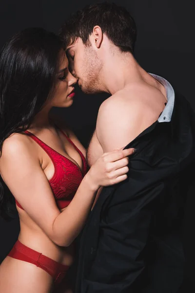 Passionnée jeune femme en sous-vêtements rouges déshabiller homme isolé sur noir — Photo de stock