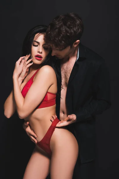 Hombre apasionado tocando bragas rojas de chica seductora aislado en negro - foto de stock