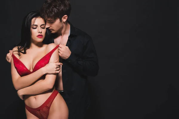 Passionate man touching red bra of seductive girl on black — Stock Photo