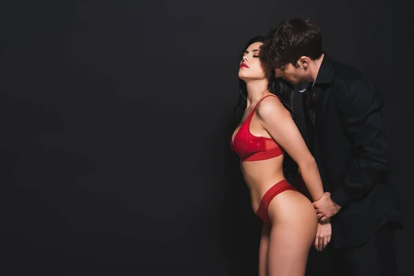 Homme dominant touchant les mains de la femme soumise en lingerie rouge sur noir — Photo de stock
