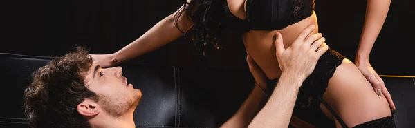 Recorte horizontal de mujer seductora en ropa interior sexy cerca de hombre aislado en negro - foto de stock