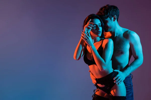 Muscular man touching seductive woman in lingerie and stockings on purple — Stock Photo