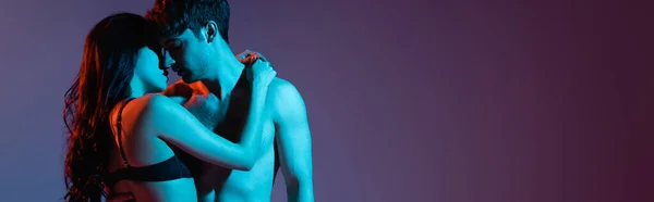 Horizontales Bild einer verführerischen Frau in Dessous, die einen muskulösen Mann auf lila umarmt — Stockfoto