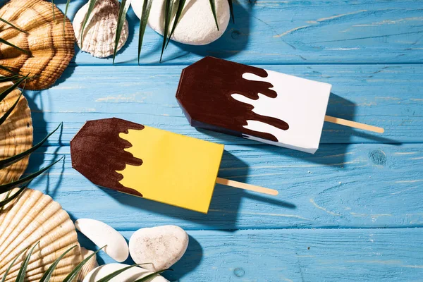 Верхний вид ракушек и пальмовых листьев возле мороженого на деревянном синем фоне — стоковое фото