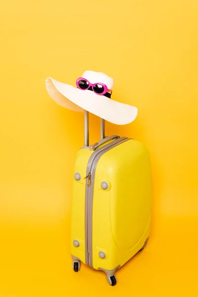 Cappello da sole e occhiali da sole su manico valigia su sfondo giallo — Foto stock