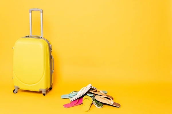 Sac de voyage avec des tongs colorées sur fond jaune — Photo de stock