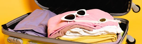 Open travel bag with summer clothes and accessories on yellow background, panoramic shot — Stock Photo