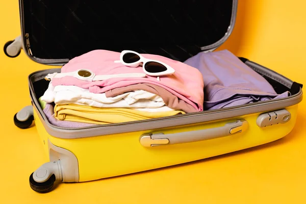 Bolsa de viaje abierta con ropa de verano y accesorios sobre fondo amarillo - foto de stock