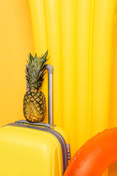 Vista de cerca de la bolsa de viaje con piña cerca de flotadores de la piscina sobre fondo amarillo - foto de stock