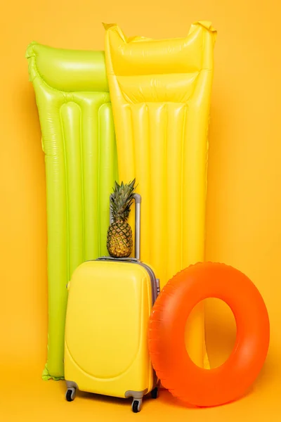 Travel bag with pineapple near pool floats on yellow background — Stock Photo