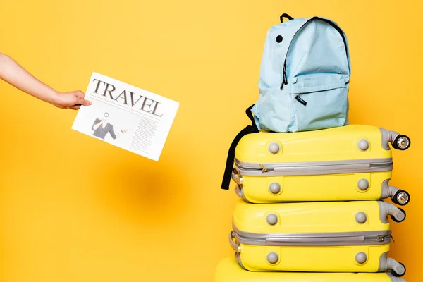 Vista recortada de la mujer sosteniendo periódico de viaje cerca de la mochila azul en bolsas de viaje en amarillo - foto de stock