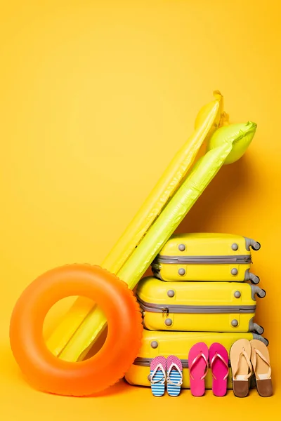 Sacs de voyage avec tongs familiales et flotteurs de piscine sur jaune — Photo de stock