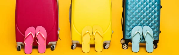 Yellow, pink and blue travel bags with flip flops isolated on yellow, panoramic shot — Stock Photo