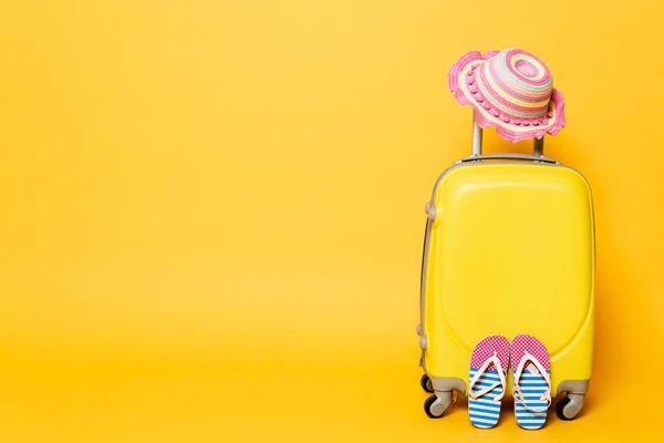 Gelbe Reisetasche mit Kindersonnenhut und Flip-Flops isoliert auf gelb — Stockfoto