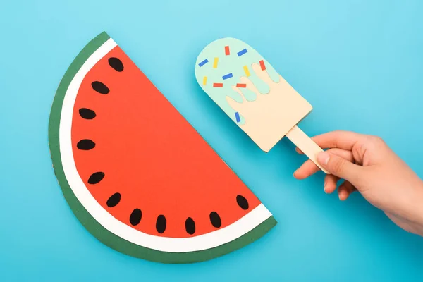 Vista recortada de la mujer sosteniendo helado de papel con aspersiones cerca de la sandía sobre fondo azul - foto de stock