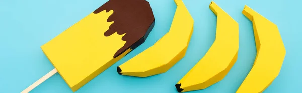 Draufsicht auf Papier gelbe Bananen und Eis auf blauem Hintergrund, Panoramaaufnahme — Stockfoto