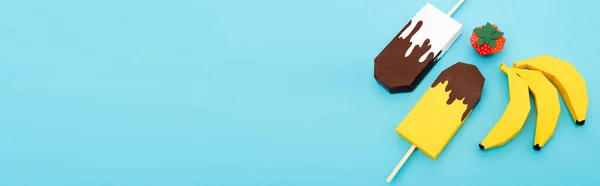 Vue du dessus de bananes en papier, fraise et crème glacée sur fond bleu, panoramique — Photo de stock