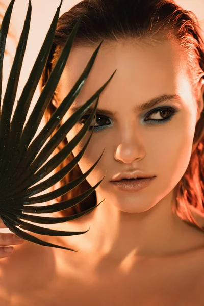 Крупним планом красива жінка з макіяжем, що дивиться в сторону пальмового листа — стокове фото