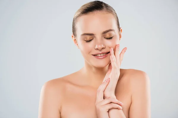 Mujer feliz y desnuda con los ojos cerrados tocando la cara aislada en gris - foto de stock