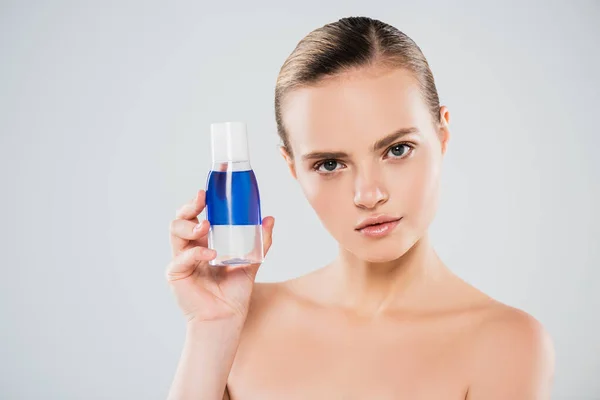 Ernste und nackte Frau mit Flasche mit Toner isoliert auf grau — Stockfoto