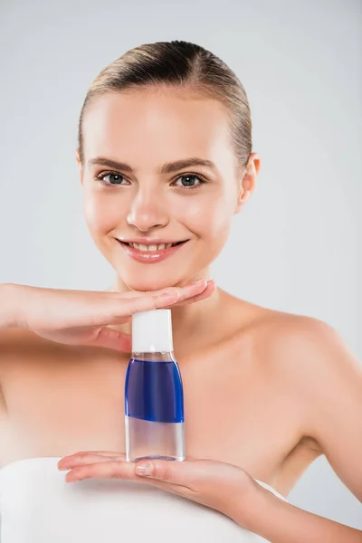 Mulher feliz segurando garrafa com toner e olhando para a câmera isolada no cinza — Fotografia de Stock