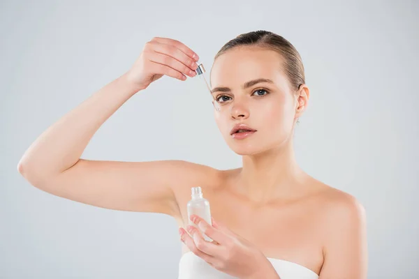 Attrayant femme tenant bouteille et l'application de sérum isolé sur gris — Photo de stock