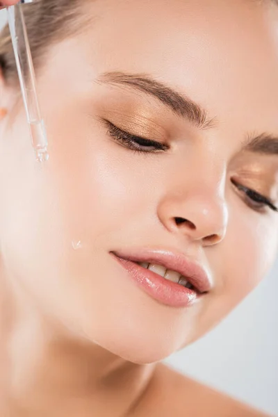 Nahaufnahme einer fröhlichen Frau, die eine Pipette hält und Serum isoliert auf grau aufträgt — Stockfoto