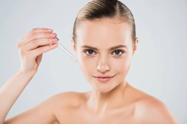 Happy young woman holding pipette with serum isolated on grey — Stock Photo