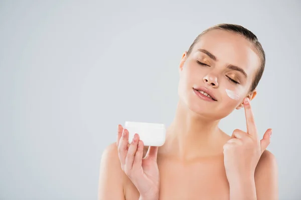 Mulher feliz segurando recipiente ao aplicar creme facial isolado no cinza — Fotografia de Stock