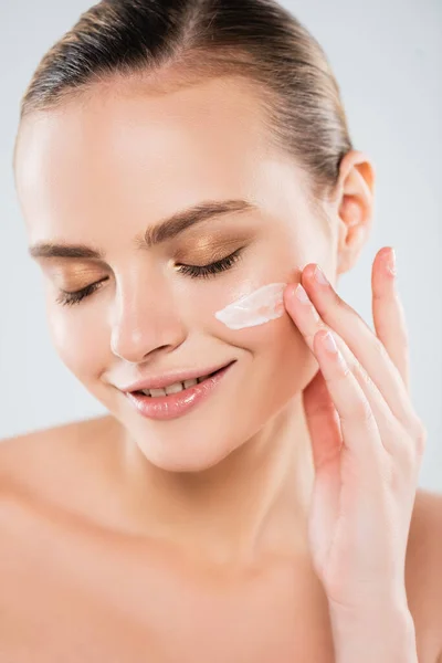 Cheerful woman with closed eyes applying face cream isolated on grey — Stock Photo