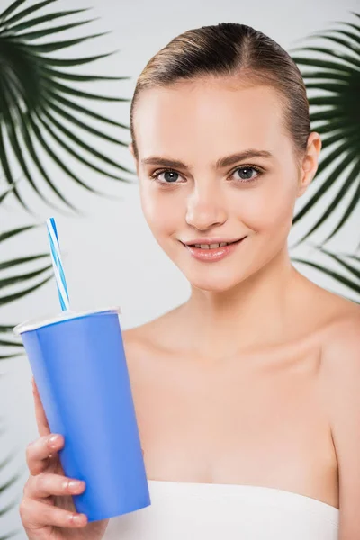 Mujer feliz sosteniendo taza desechable con paja cerca de hojas de palma en blanco — Stock Photo