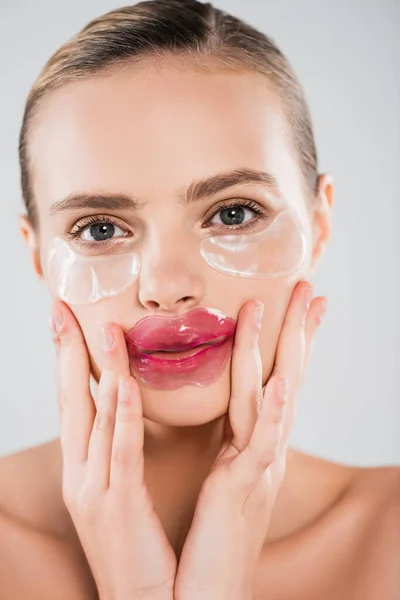 Belle femme avec masque à lèvres et patchs pour les yeux touchant visage propre isolé sur gris — Photo de stock
