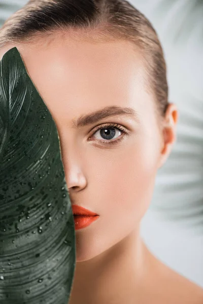 Atractiva mujer con maquillaje mirando a la cámara cerca de hoja verde y húmedo en blanco - foto de stock