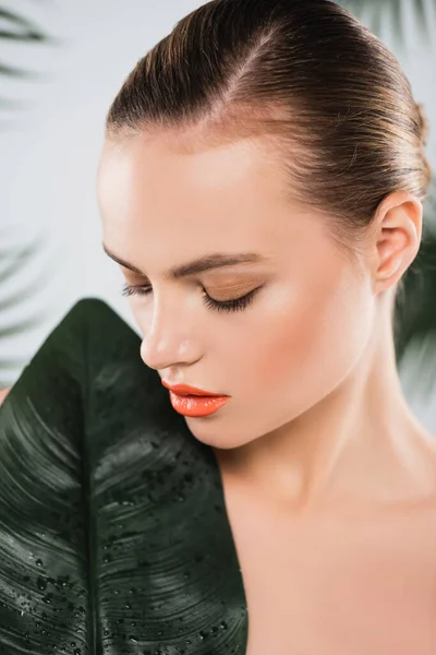 Atractiva mujer con maquillaje mirando la hoja verde en blanco - foto de stock