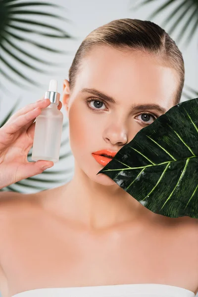 Attractive woman holding bottle with serum near leaf on white — Stock Photo