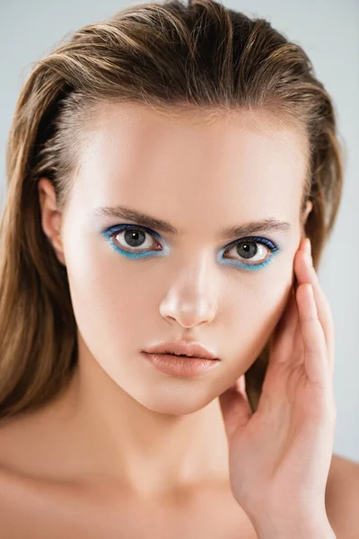 Nudo giovane donna con ombretto blu toccare viso isolato su bianco — Foto stock