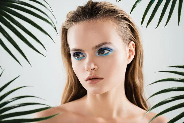 Beautiful woman with blue eye shadow near palm leaves on white — Stock Photo