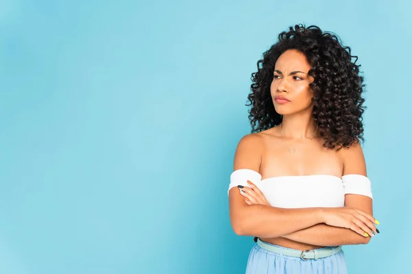Displeased african american girl standing with crossed arms and looking away on blue — Stock Photo