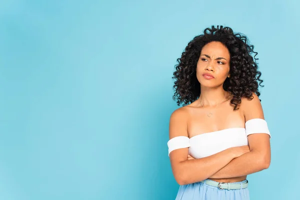 Displeased african american woman standing with crossed arms and looking away on blue — Stock Photo