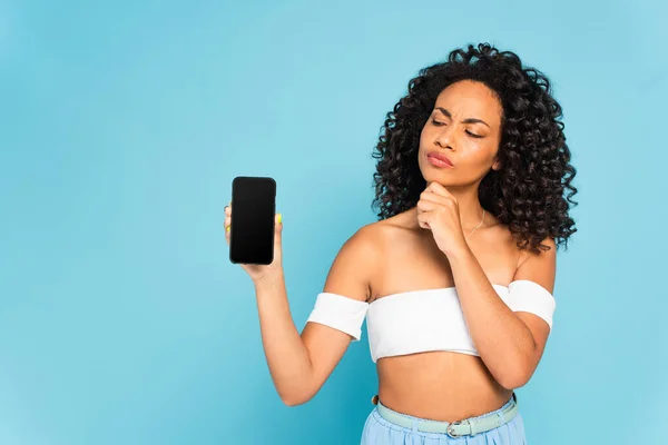 Стомлена афроамериканська дівчина дивиться на смартфон з порожнім екраном ізольовано на синьому — стокове фото