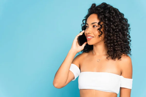 Chica afroamericana feliz hablando en teléfono inteligente aislado en azul - foto de stock