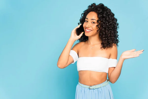 Menina americana africana feliz falando no smartphone e gesticulando isolado no azul — Fotografia de Stock