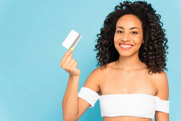 Happy and curly african american woman holding credit card isolated on blue — Stock Photo