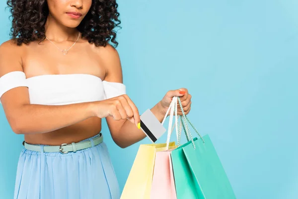 Vista recortada de chica afroamericana con tarjeta de crédito y bolsas de compras en azul - foto de stock