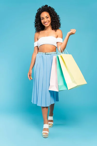 Fröhliches afrikanisch-amerikanisches Mädchen läuft und hält Einkaufstüten auf blauem Grund — Stockfoto
