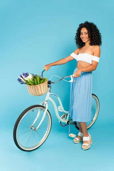 Cheerful african american girl standing with bicycle on blue, summer concept — Stock Photo