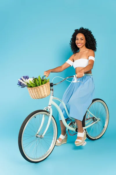 Cheerful african american girl riding bicycle on blue, summer concept — Stock Photo